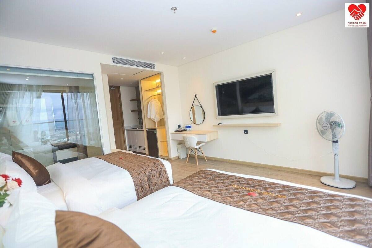 Une chambre d’hôtel avec deux lits, un bureau, une chaise, une télévision et un ventilateur sur pied.