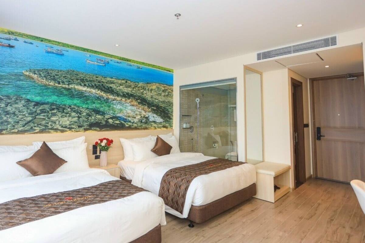 Une chambre d’hôtel avec deux lits, une grande fresque représentant un paysage côtier, une cabine de douche en verre et une porte en bois.