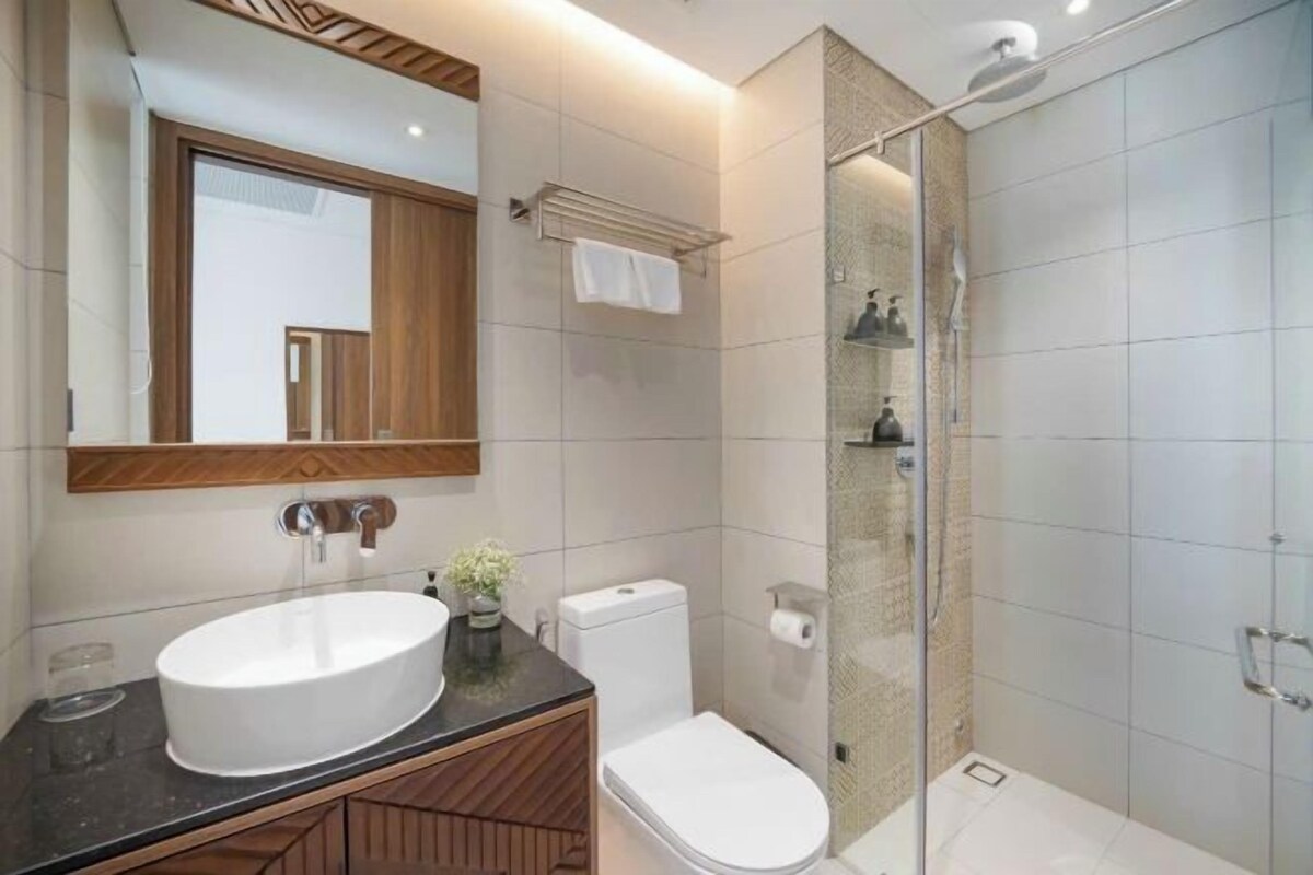 A modern bathroom with a double sink, toilet, and a glass-enclosed shower.