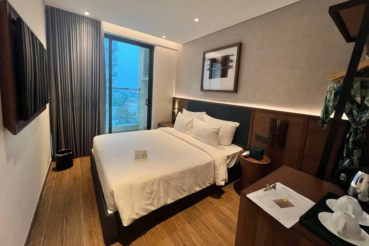 Une chambre d’hôtel moderne, dotée d’un grand lit, d’un bureau et offrant une vue sur la ville grâce à une grande fenêtre.