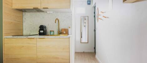 A compact kitchen with wooden cabinets, a countertop, and a sink. There is a bed with a white headboard in the foreground.