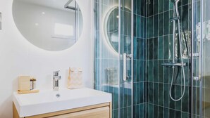 A modern bathroom with a white sink, wooden cabinet, and a glass-enclosed shower area with a handheld showerhead. - Modern "green Suites" Residence - Meudon/velizy (Meudon)