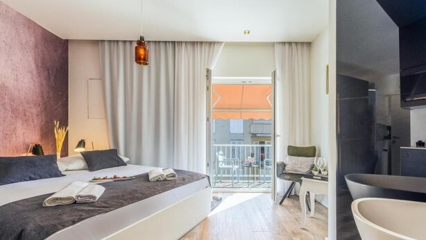A modern hotel room with a large bed, a balcony with a view, a bathroom with a bathtub, and a dining area with a table and chairs. - Luxury rooms in Old Town (Zadar)