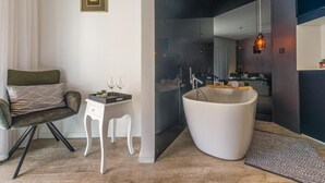 A modern bathroom with a freestanding bathtub, a vanity with a mirror, and a small seating area with a chair and a table. - Luxury rooms in Old Town (Zadar)