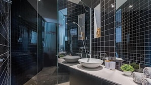 A modern bathroom with two large white sinks, a glass shower enclosure, and a dark tiled wall. - Luxury rooms in Old Town (Zadar)