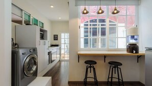 A compact kitchen with a built-in washer, a window with a view, and two bar stools.