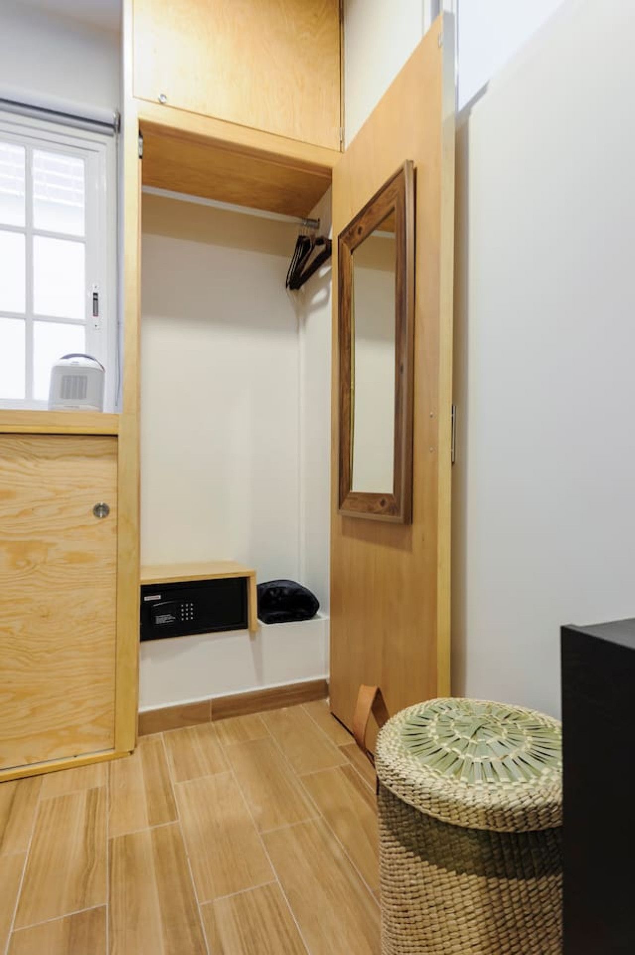A compact bathroom with a wooden cabinet, a black heater, a woven stool, and a mirror on the wall.