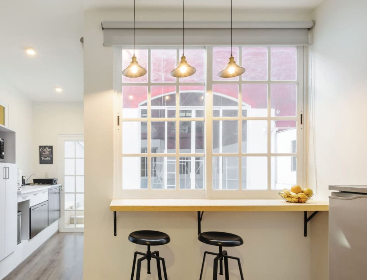 Eine moderne Küche mit großem Fenster, zwei Barhocker und hängenden Pendelleuchten.