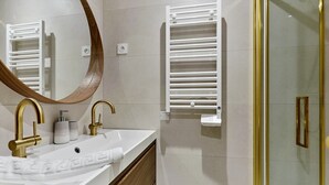 A bathroom with a white sink, gold faucets, a mirror, and a towel rack.
