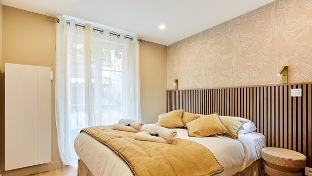 A neatly arranged bedroom with a bed, bedside tables, a radiator, and a window with curtains.
