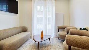 A living room with a sofa, armchairs, a coffee table, and a TV mounted on the wall.