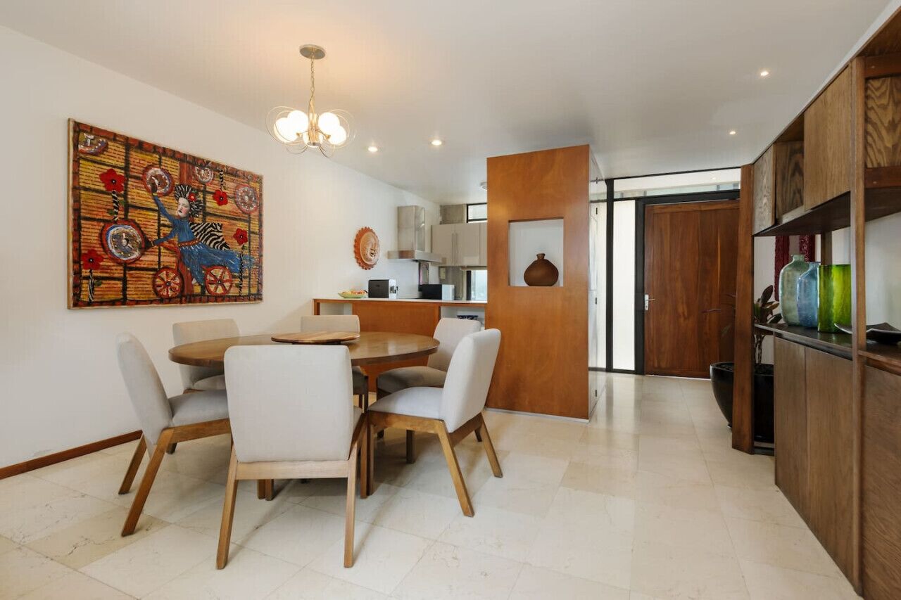 Une cuisine moderne avec des meubles en bois, un coin repas avec une table ronde et des chaises, et un grand tableau décoratif au mur.