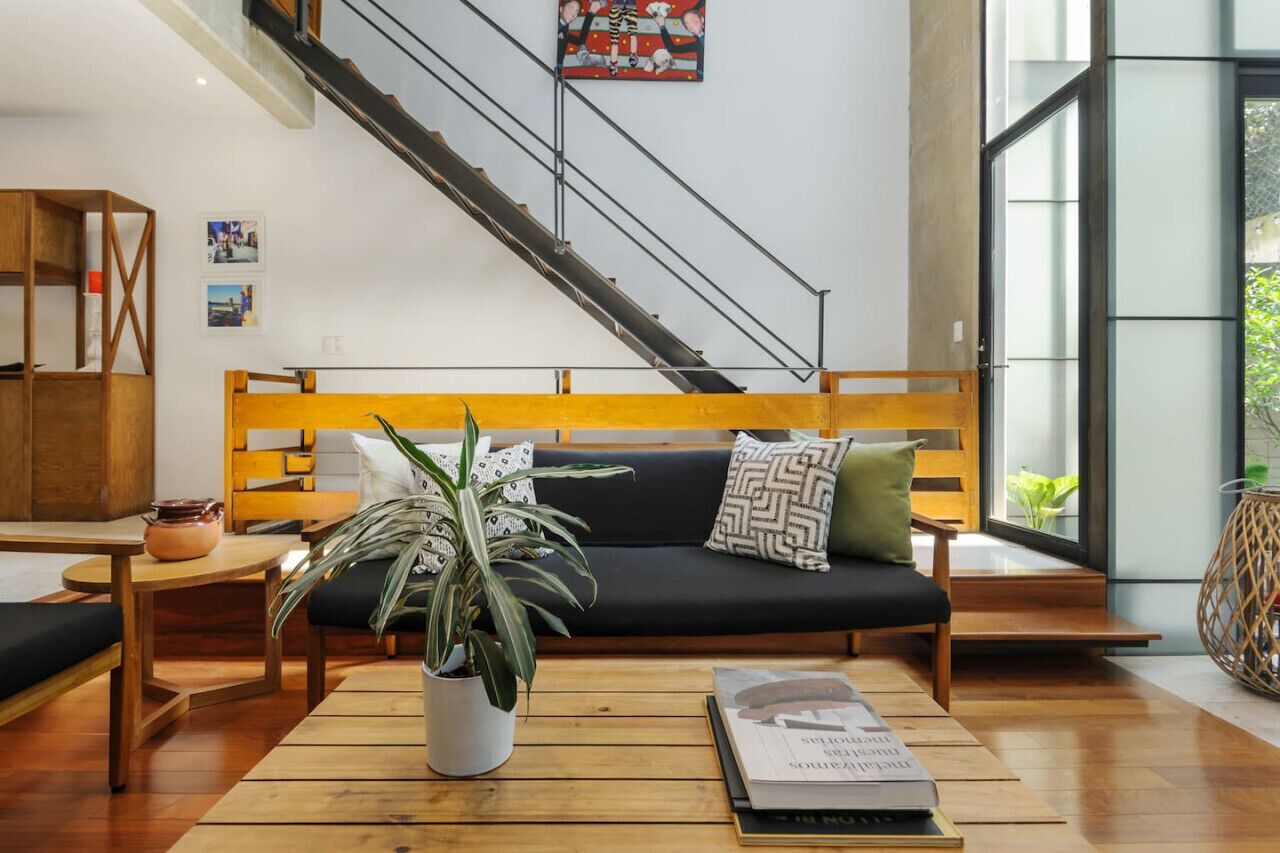 Una sala moderna con un banco de madera, una mesita de centro, una planta en maceta y una escalera.