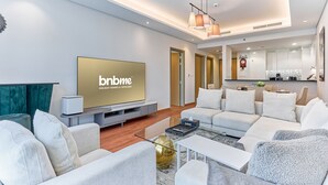 Een moderne woonkamer met een grote flatscreen-tv, comfortabele zithoek, salontafel en een keuken in de achtergrond.