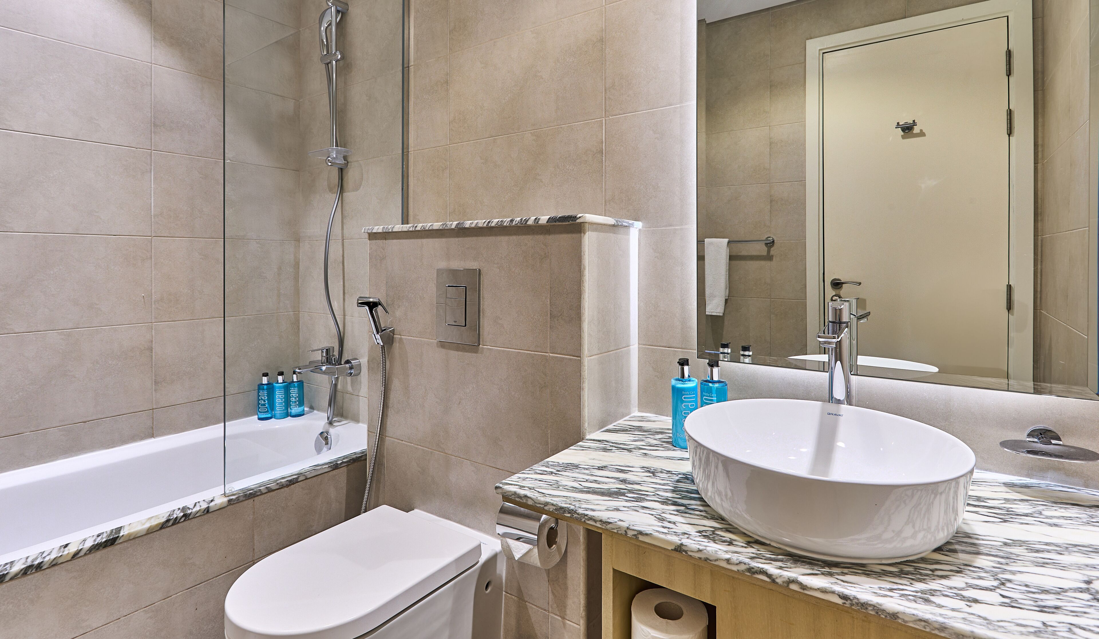 A bathroom with a bathtub, a sink with a large basin, and a toilet. There are toiletries on the counter.