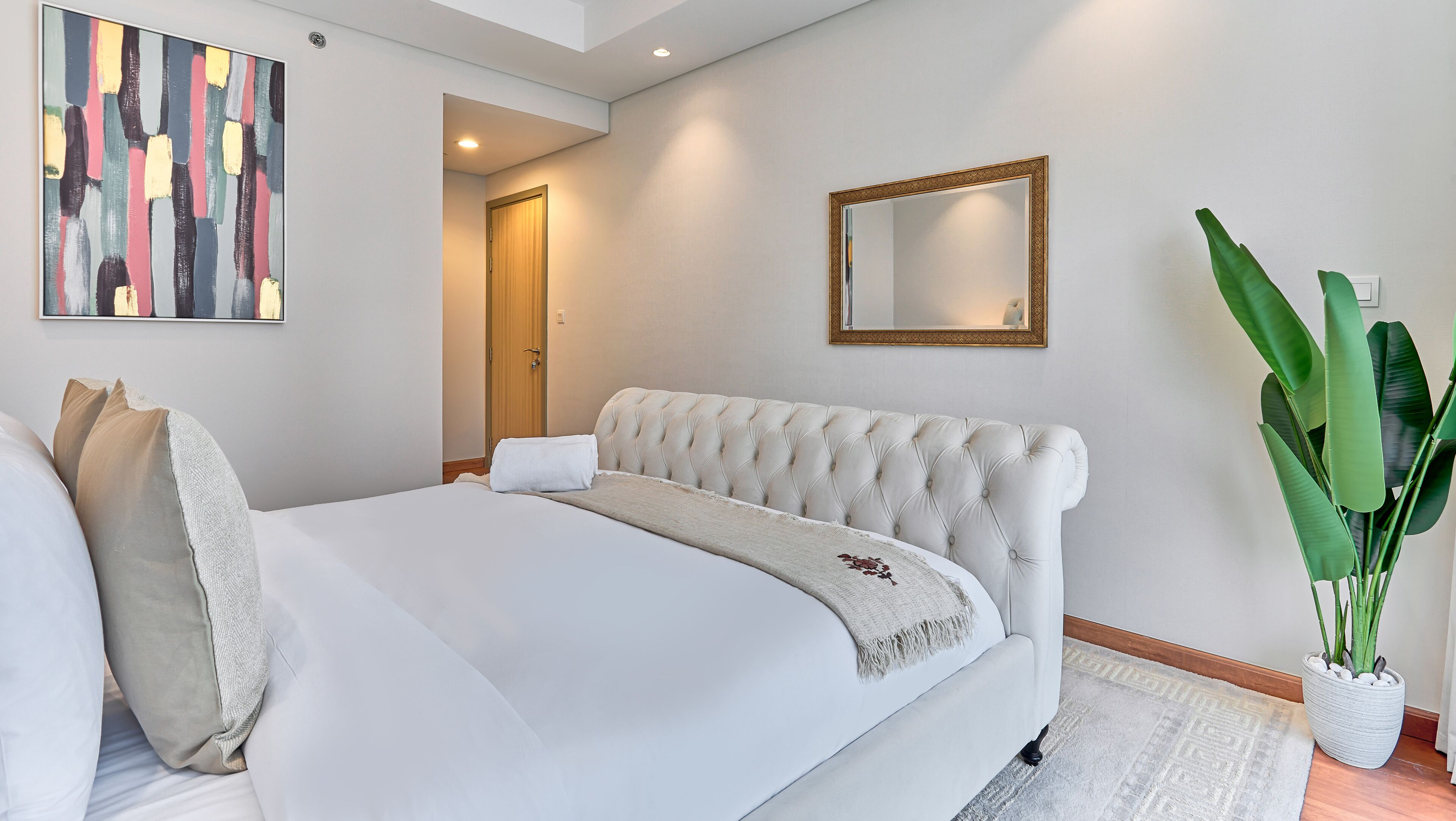 A bedroom with a large bed, a mirror, a painting, and a potted plant.