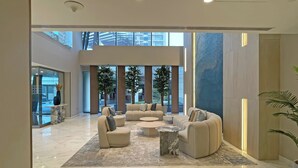 A spacious lobby with a high ceiling, large windows, and a seating area with sofas and a coffee table.