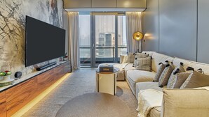 A modern living room with a flat-screen TV mounted on a marble wall, a sofa with patterned cushions, a small side table, and a view of the city through large windows.
