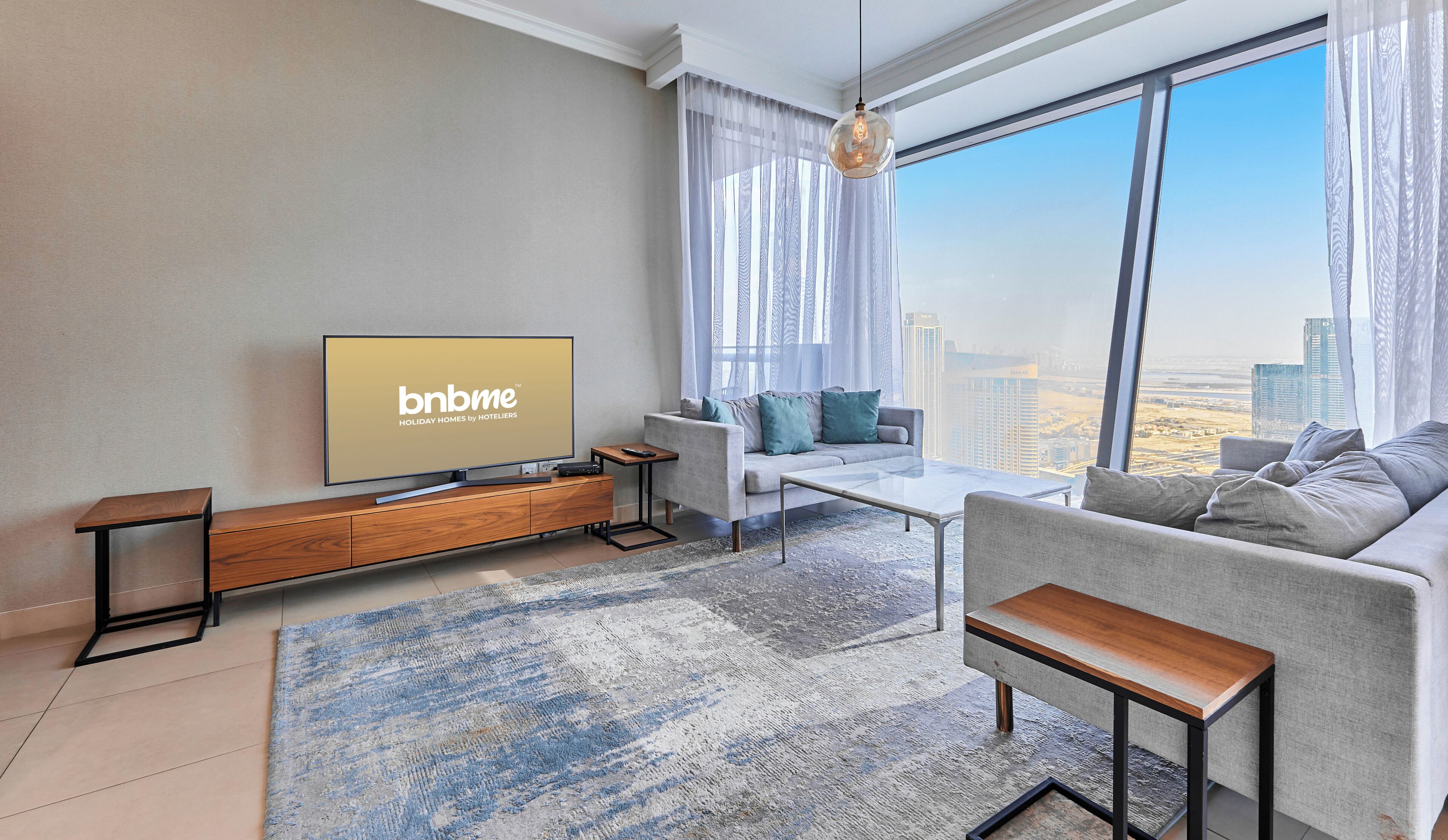 Ein modernes Wohnzimmer mit großem Fernseher, einer Couch, einem Couchtisch und Blick auf eine Stadtkulisse durch große Fenster.