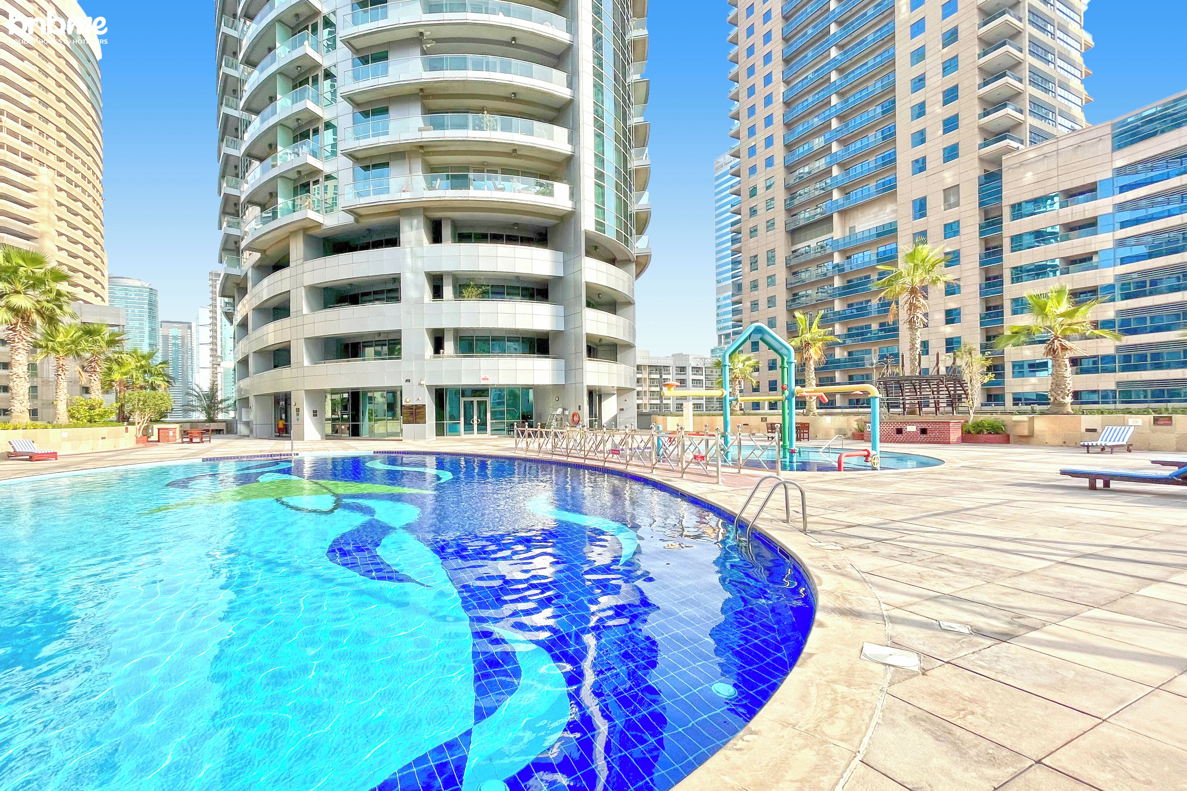 A modern hotel with a swimming pool, high-rise buildings, and palm trees.