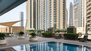 A swimming pool area with lounge chairs and potted plants, surrounded by high-rise buildings. - bnbme | 8 Boulevard Walk | Studio (Dubai)