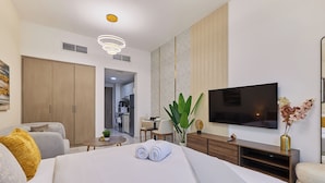 Una habitación de hotel moderna con una cama grande, televisión, escritorio y una kitchenette al fondo.
