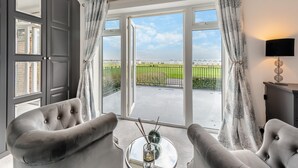 Ein geräumiges Zimmer mit einem großen Schiebeglasfenster zum Balkon, zwei bequemen Ohrensesseln, einem kleinen runden Tisch mit Glasplatte und einer modernen Lampe.