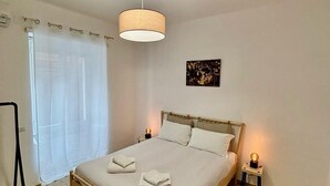 Une chambre à coucher avec un lit, un luminaire suspendu, une table de chevet avec une lampe et une fenêtre avec des rideaux.