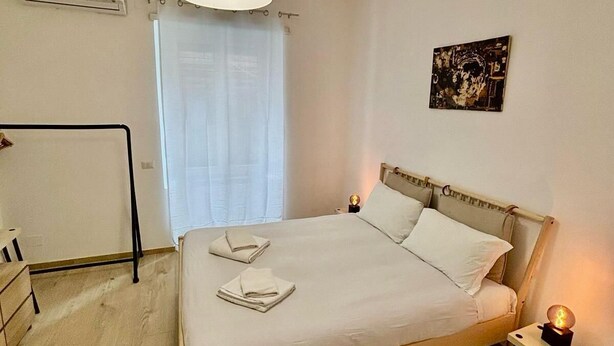 Un lit bien fait, avec des serviettes pliées, une lampe de chevet et un climatiseur fixé au mur.