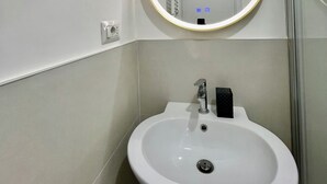 Une salle de bain avec un lavabo blanc, un miroir avec un cadre doré et une porte dotée d’une poignée.