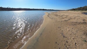 Une plage à l’eau claire, avec un rivage sablonneux et une ligne d’arbres à l’horizon, le tout baigné par un soleil éclatant.