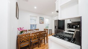 Una cocina moderna con muebles blancos, estufa a gas y un comedor con sillas de madera y un jarrón de flores.
