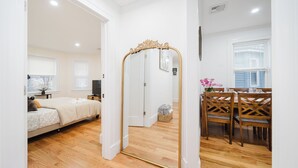 Una habitación con cama, suelo de madera, mesa de comedor con sillas y espejo con marco decorativo.