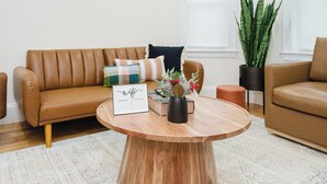 Una sala de estar moderna con un sofá de cuero marrón, una mesa de centro redonda de madera y una planta en maceta.