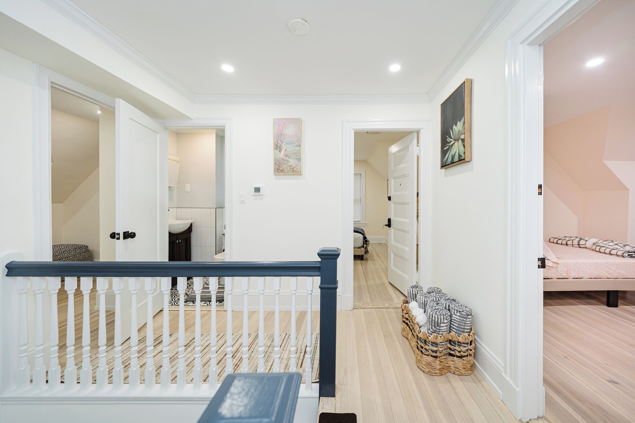 Un couloir avec un escalier, des murs blancs et un lit recouvert d’une couvre-lit à motifs.