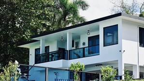 A modern two-story house with a balcony, large windows, and a garden area. - Private Pickleball Oasis + Pool + 15 Min to Beaches & El Yunque, 30 Min Airport (Río Grande)