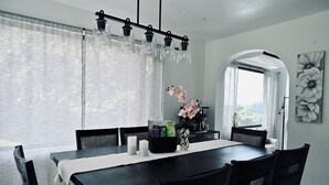 A dining area with a dark wooden table, white tablecloth, and black chairs. There is a vase with pink flowers on the table. - Private Pickleball Oasis + Pool + 15 Min to Beaches & El Yunque, 30 Min Airport (Río Grande)