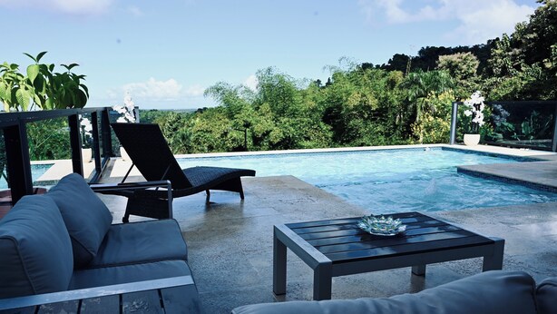 A poolside area with lounge chairs and a table, surrounded by lush greenery and a clear view of the landscape. - Private Pickleball Oasis + Pool + 15 Min to Beaches & El Yunque, 30 Min Airport (Río Grande)