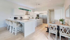 Eine moderne Küche mit weißen Schränken, einer zentralen Kochinsel und einem Essbereich mit Holztisch und weißen Stühlen.