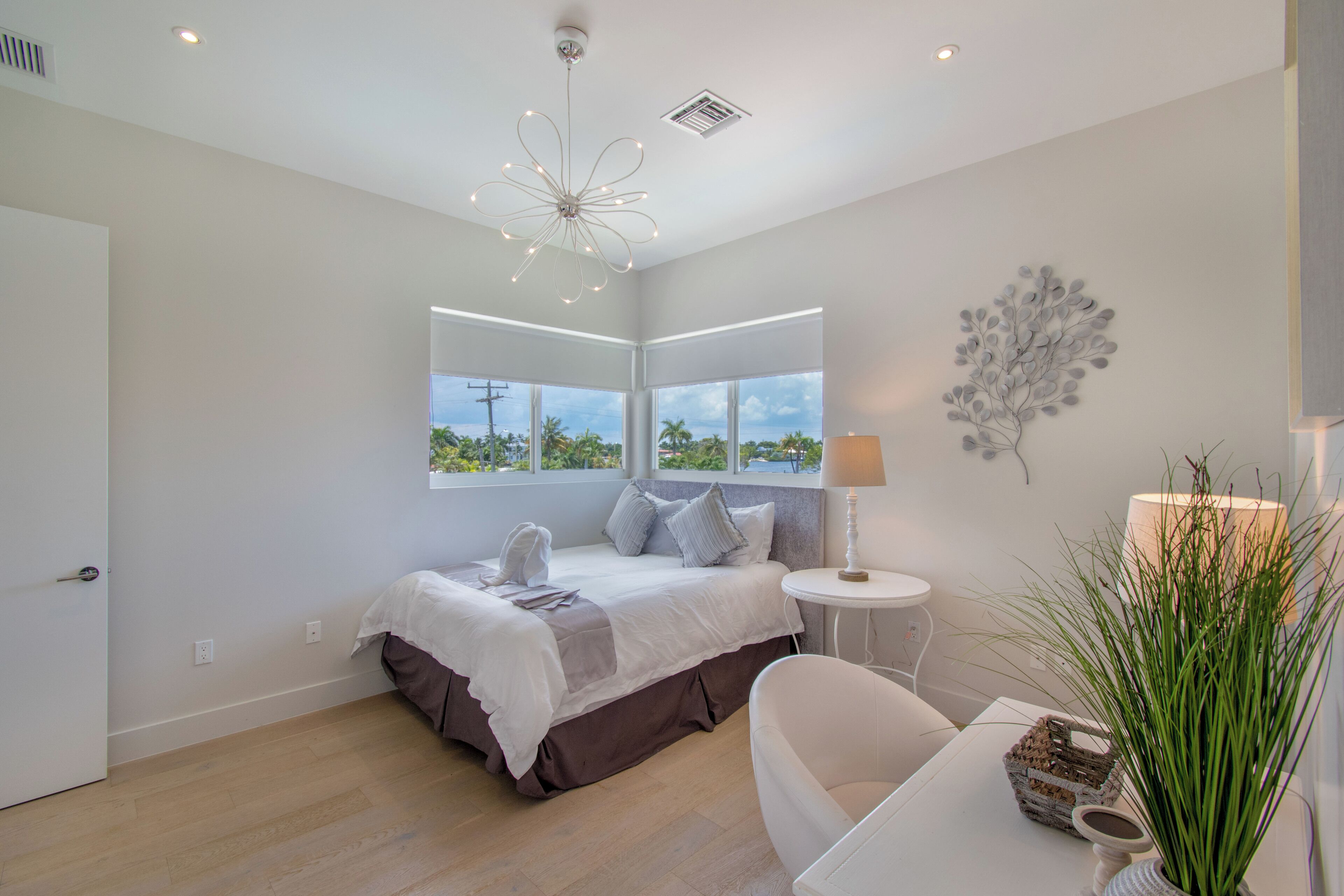 A modern bedroom with a large bed, a bedside table, a lamp, and a view of the outdoors.