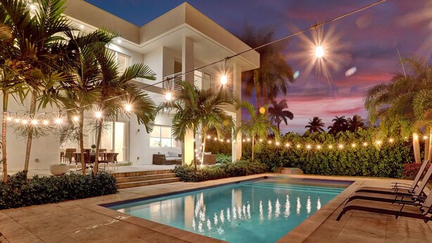 Ein modernes Haus mit Swimmingpool, Lichterkette und Palmen.