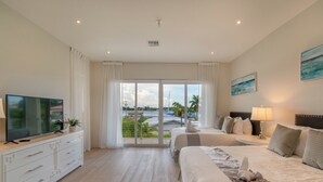 Ein Hotelzimmer mit zwei Betten, einem Fernseher, einem Schminktisch und einem Balkon mit Blick auf die Stadt.