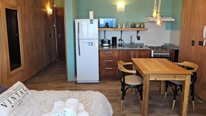 Une cuisine compacte équipée d’un réfrigérateur, d’une cuisinière et d’un évier. On y trouve une table à manger en bois avec des chaises, ainsi qu’un petit tapis sur lequel sont posées des serviettes.