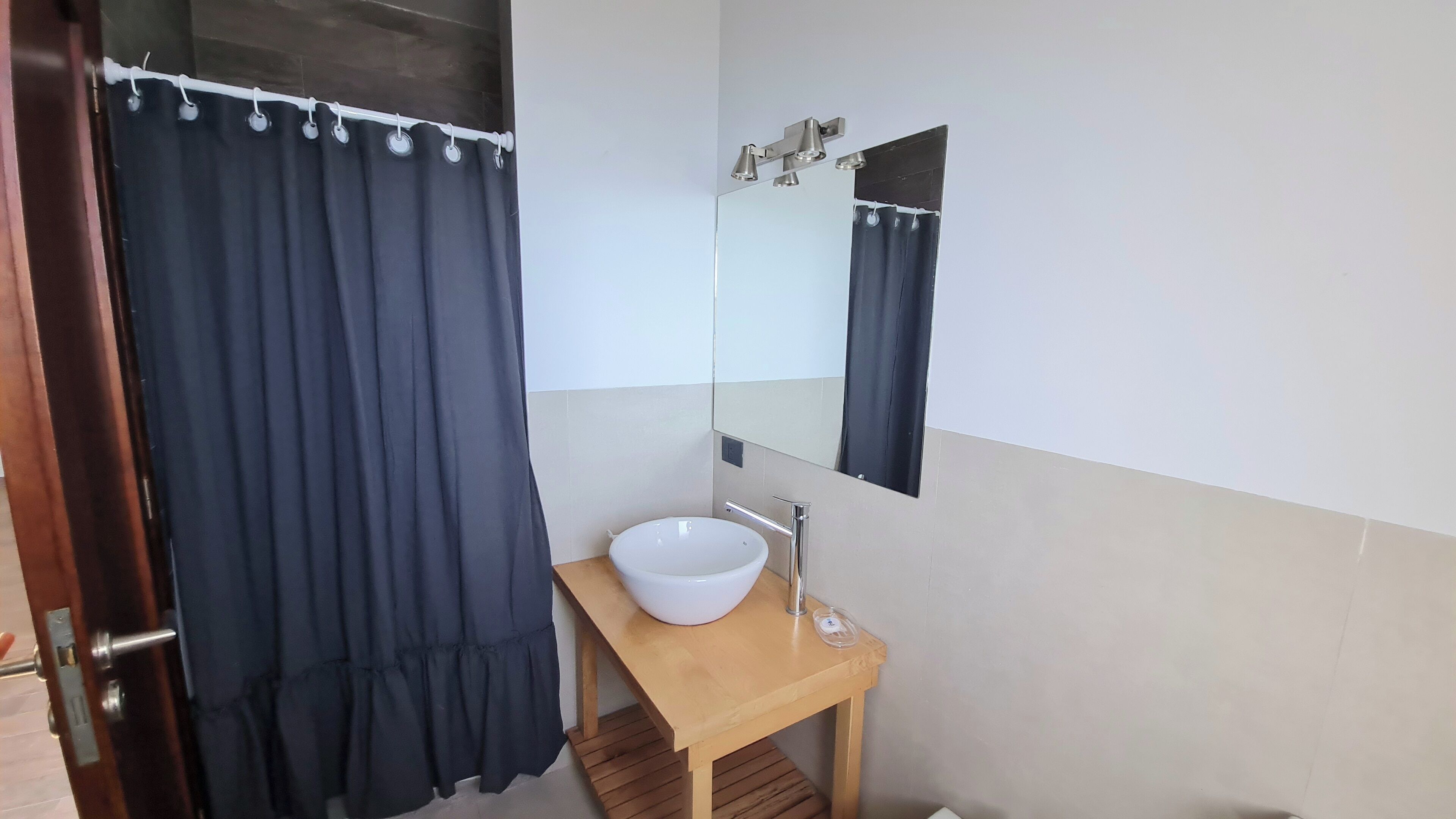 A bathroom with a wooden vanity, a white sink, a mirror, and a dark blue shower curtain.