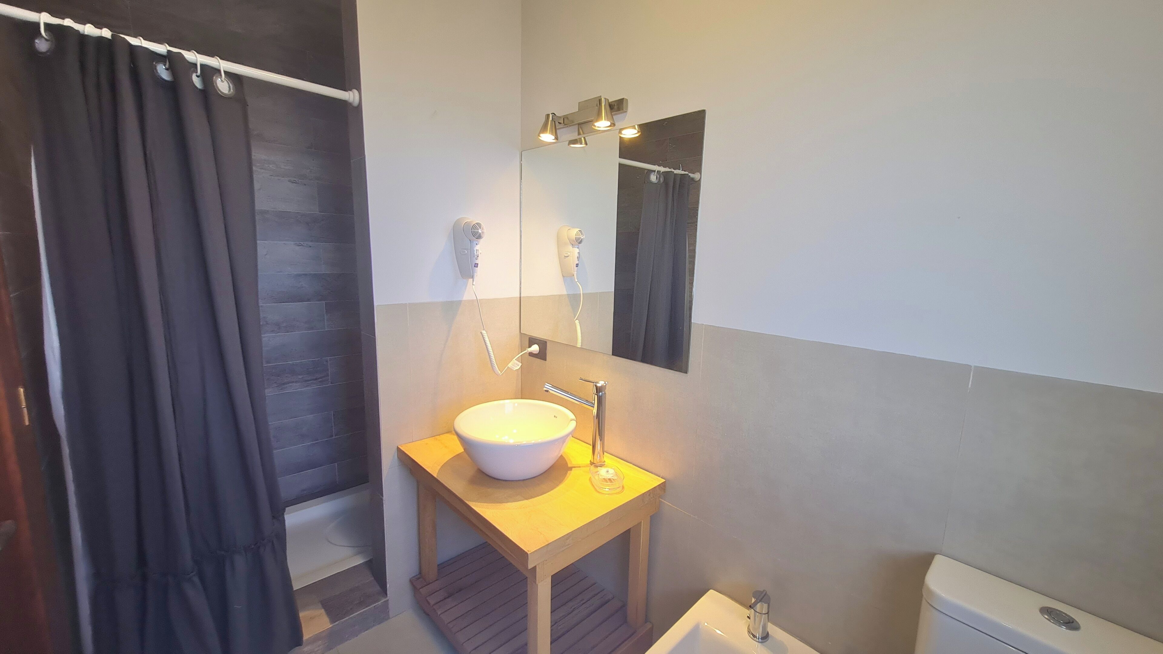 Een badkamer met een houten wastafelmeubel, een witte wastafel, een spiegel en een douchegordijn.