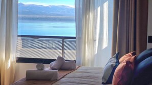Une chambre avec vue sur un lac et des montagnes. On y trouve un lit avec des oreillers et une serviette enroulée.