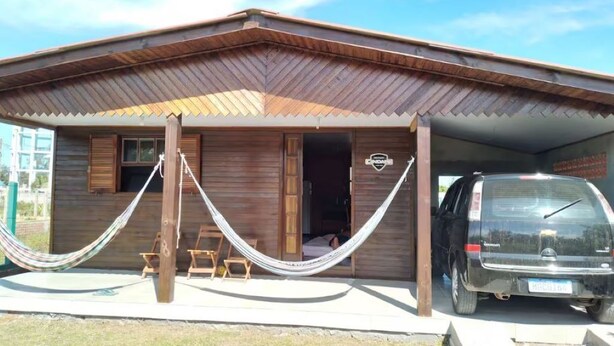 A wooden building with a covered porch, a hammock, and a parked SUV. - Nice house, one block from the sea.  (Arroio do Sal)