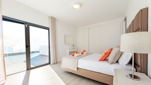 A modern hotel room with a large bed, a nightstand, a lamp, and a sliding glass door leading to a balcony.
