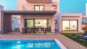 Uma casa moderna de dois andares com piscina, área de refeições ao ar livre e interior bem iluminado.