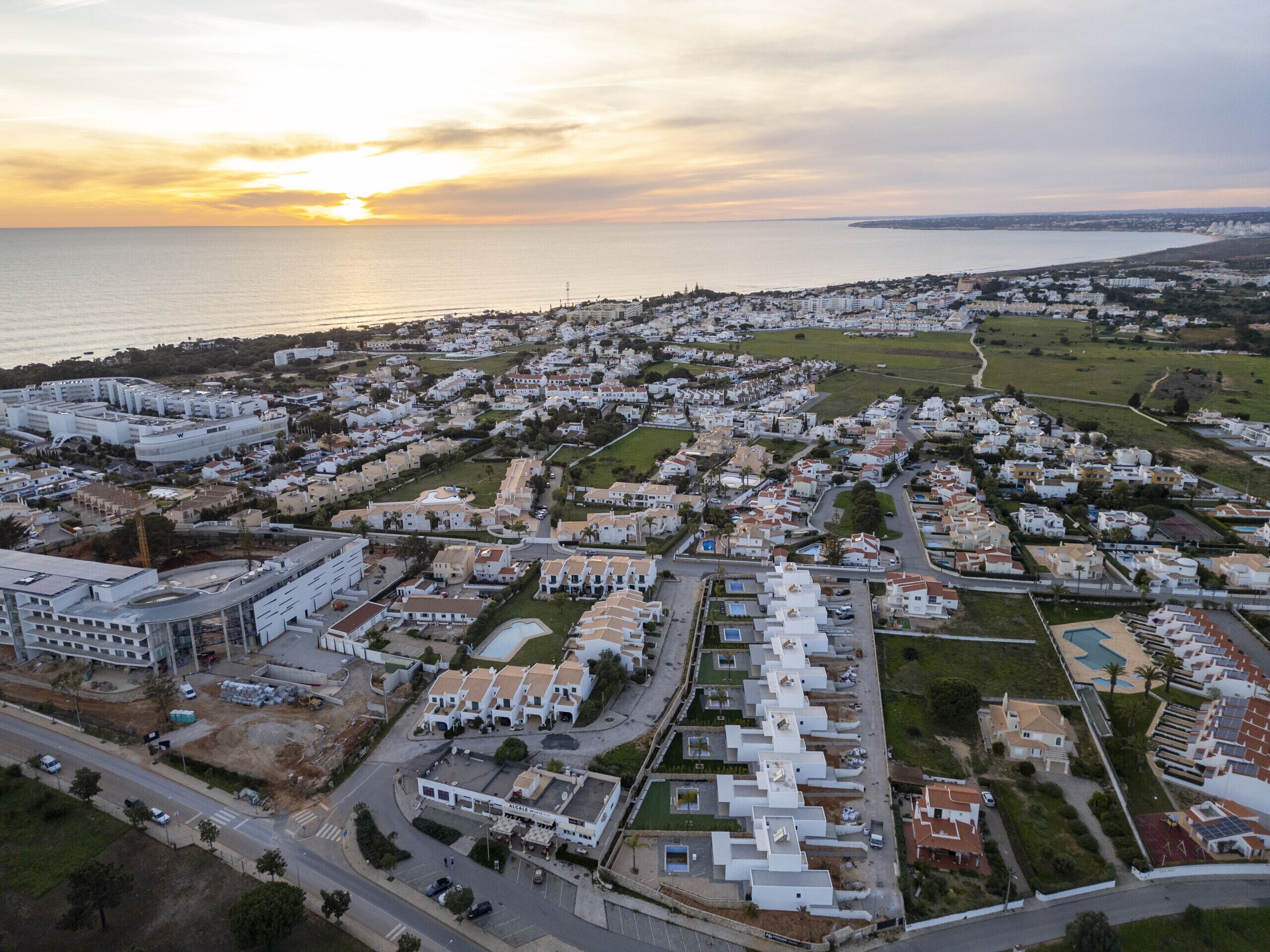 Vista aérea de una zona residencial costera con casas unifamiliares y edificios de apartamentos, destacando una avenida central y una gran extensión de agua al fondo.